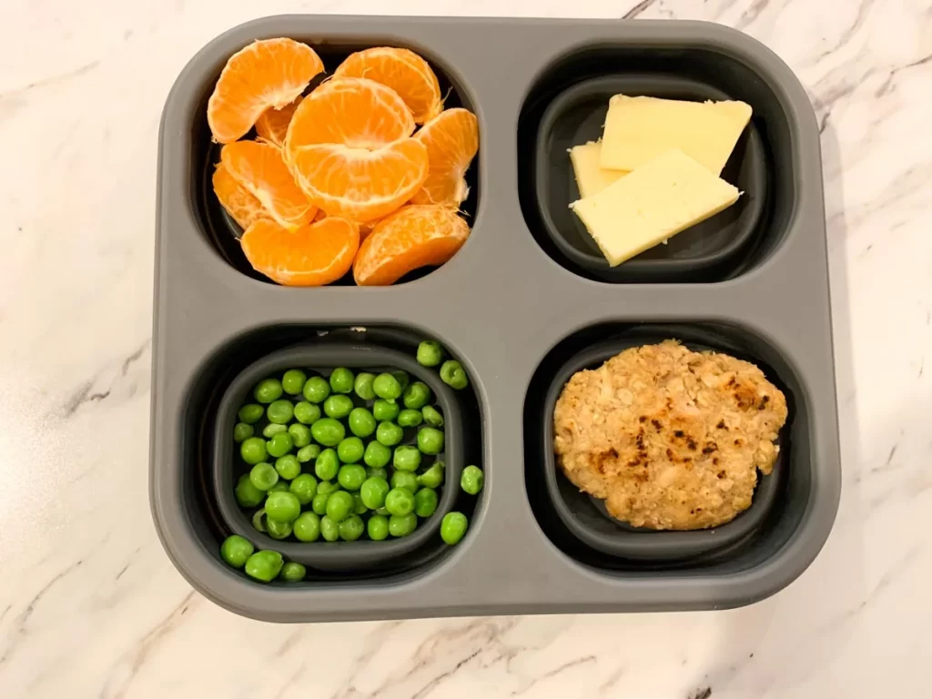 healthy toddler meal shown including oranges, peas, cheese, and tuna cake