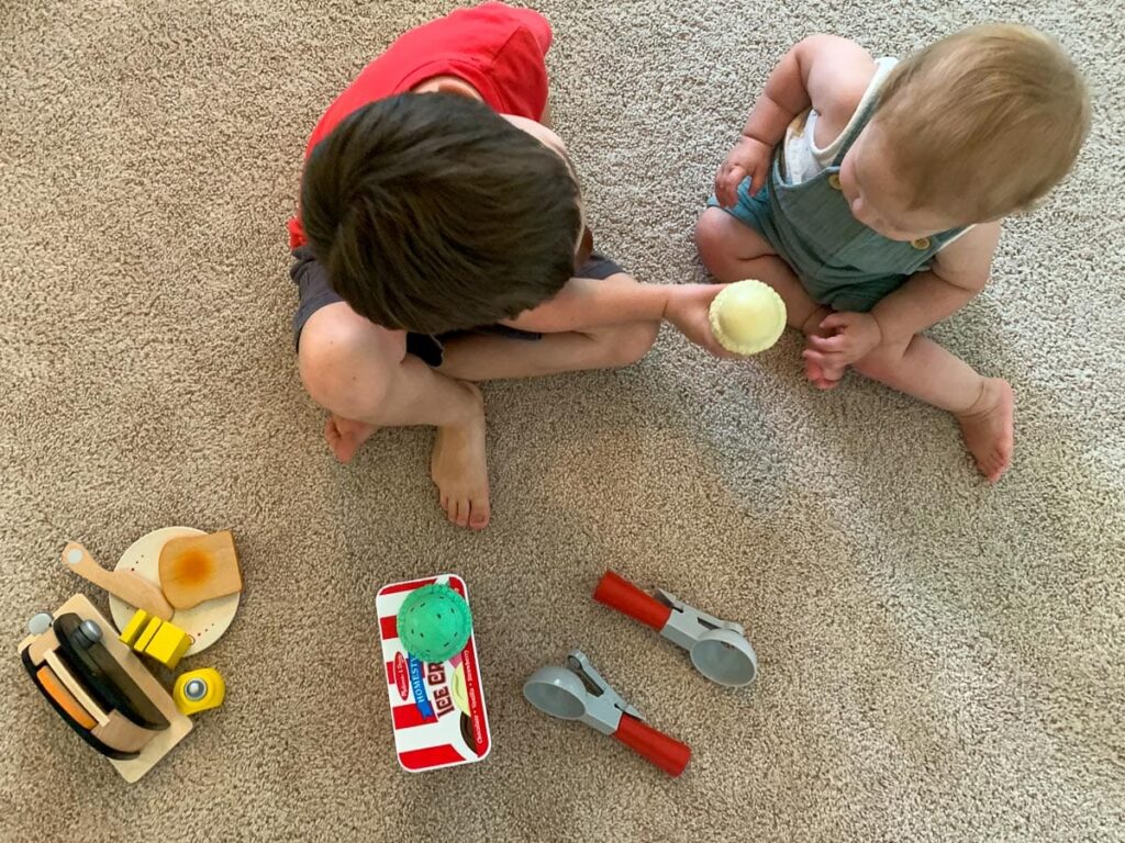 2 toddlers playing with playing with pretend food and toy food sets including a play toaster and ice cream set