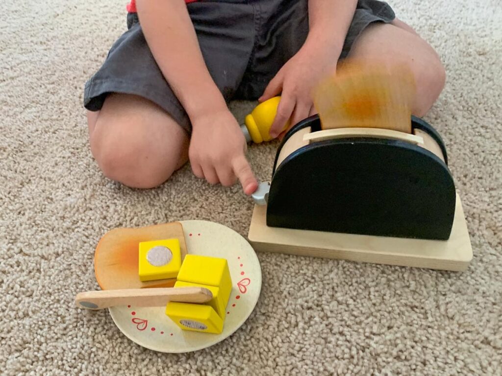 toddler pretends with a wooden toaster toy